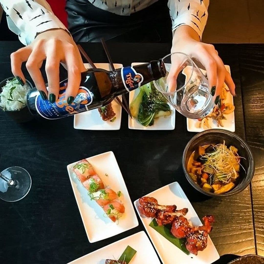 Person pouring beer into a glass with an array of Asian-Latin fusion dishes on a table at Chino Latino.