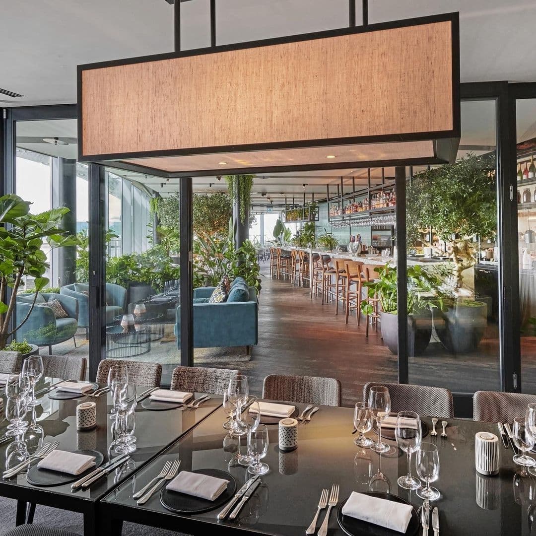 Elegant dining setup at Crafthouse with tables set with glassware and cutlery, surrounded by indoor greenery and a well-stocked bar in the background.