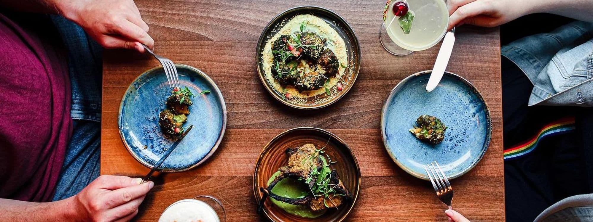Diners enjoying a variety of gourmet dishes on colorful ceramic plates at De Baga – Headingley, with a focus on a vibrant culinary experience.
