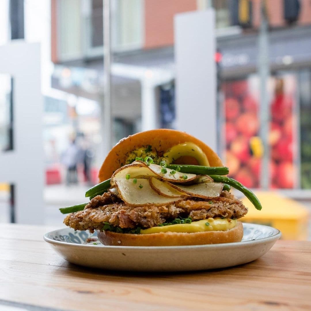 Gourmet sandwich with crispy chicken, fresh green beans, and sliced apples on a brioche bun served at Eat Your Greens.