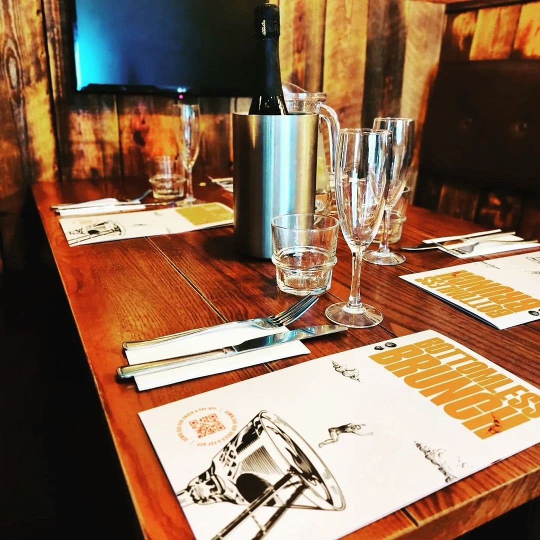 A cozy dining setup at Editor’s Draught with a wooden table laid with menus, cutlery, a bottle of wine in an ice bucket, and elegant champagne glasses, ready for a delightful meal.