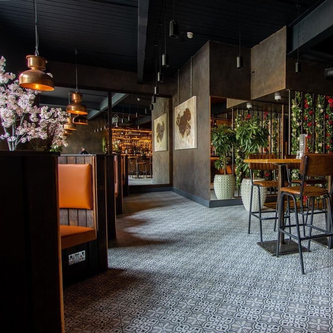 Interior of Estabulo – The Light featuring stylish seating, decorative lighting, patterned floor tiles, and vibrant plant decor.