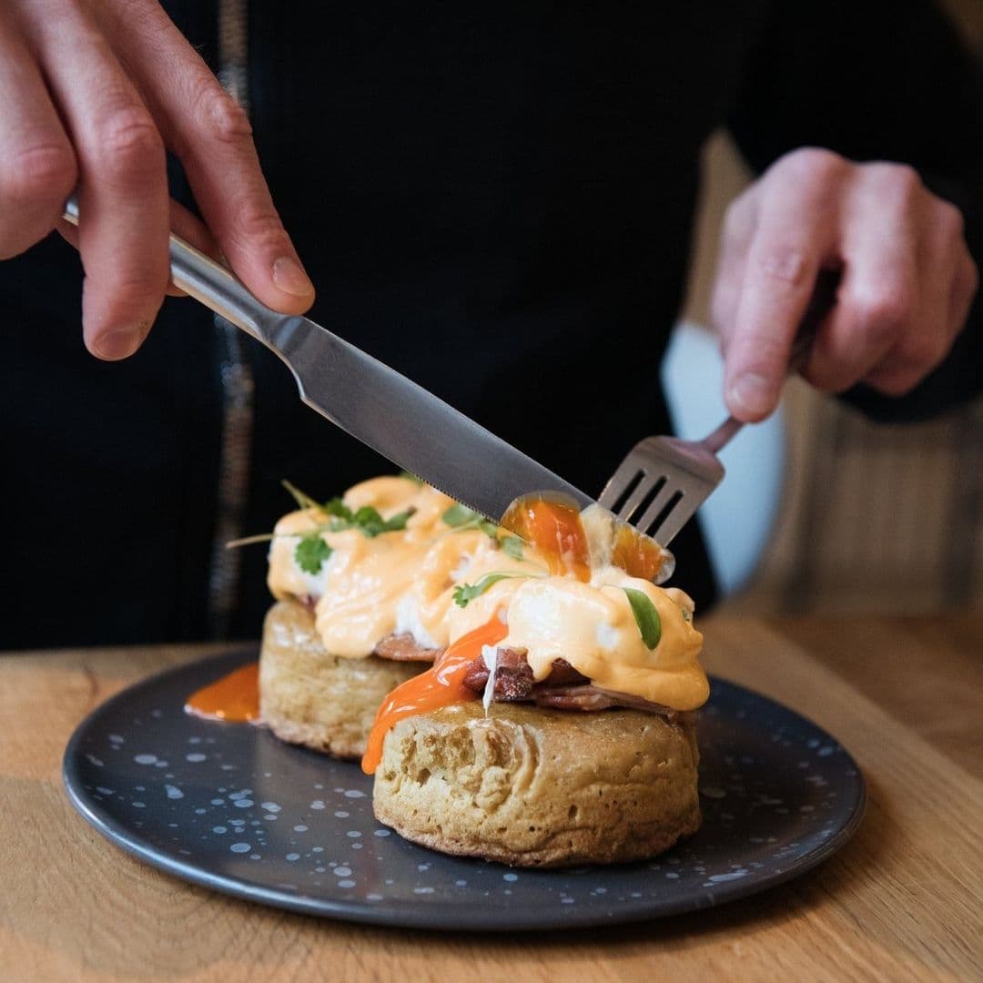 Alt text: "Delicious eggs Benedict with creamy hollandaise sauce served on a plate at FINT, ready to be enjoyed by a diner using a knife and fork."