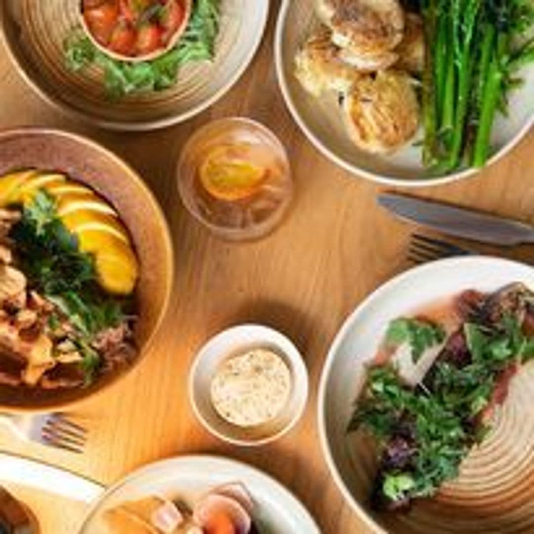 Assorted gourmet dishes on a wooden table at FINT, featuring fresh salads, grilled asparagus, succulent meats, and refreshing beverages.