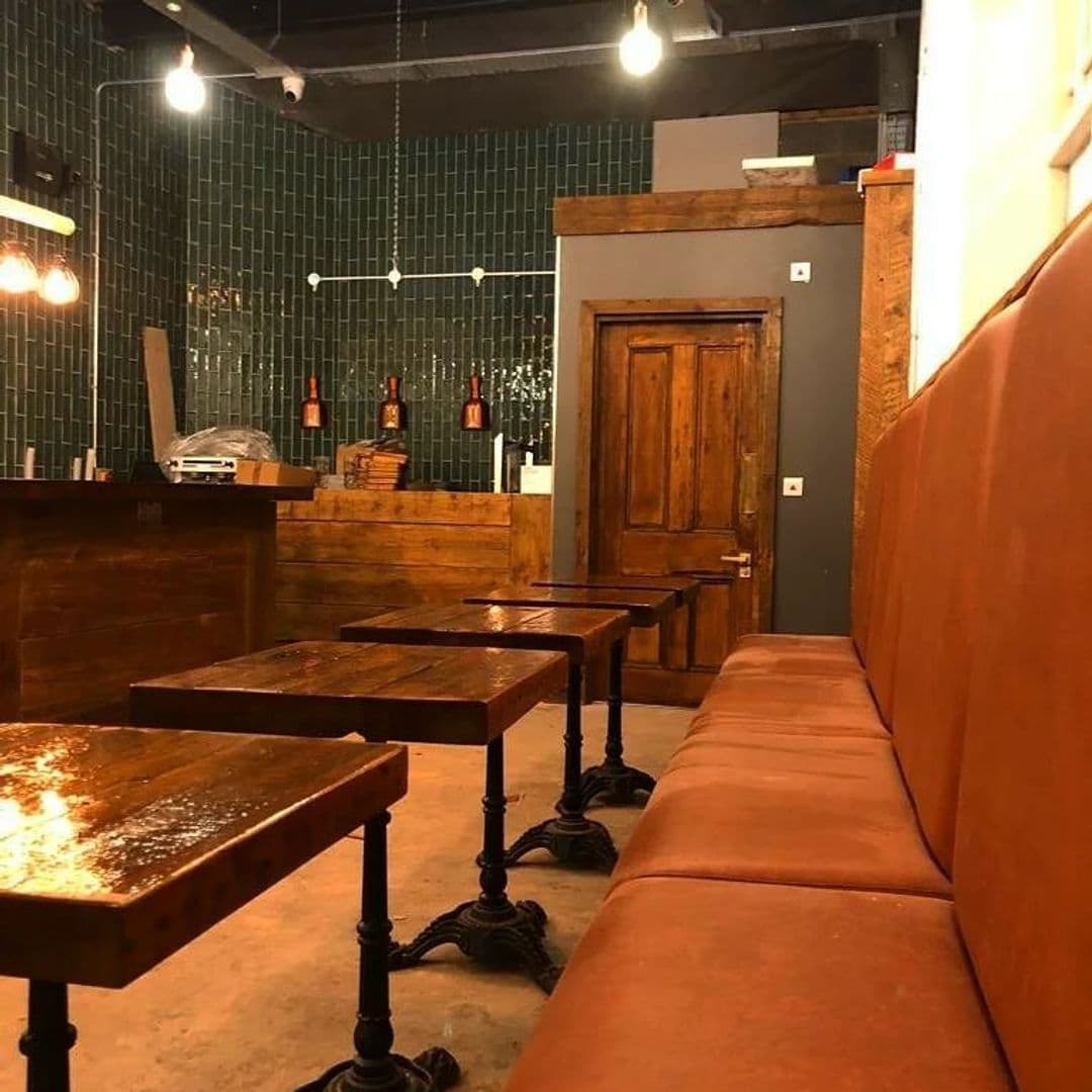 Cozy interior of a cafe in Forde with wooden tables, a long leather bench, and a bar area with hanging wine glasses.
