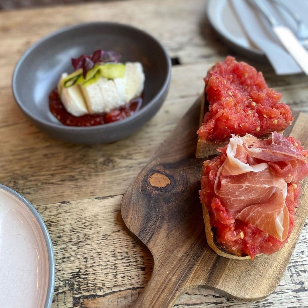 Gourmet appetizers on a wooden board featuring tomato bruschetta with cured ham and a bowl of fresh cheese with berry compote, served at a dining establishment in Forde.