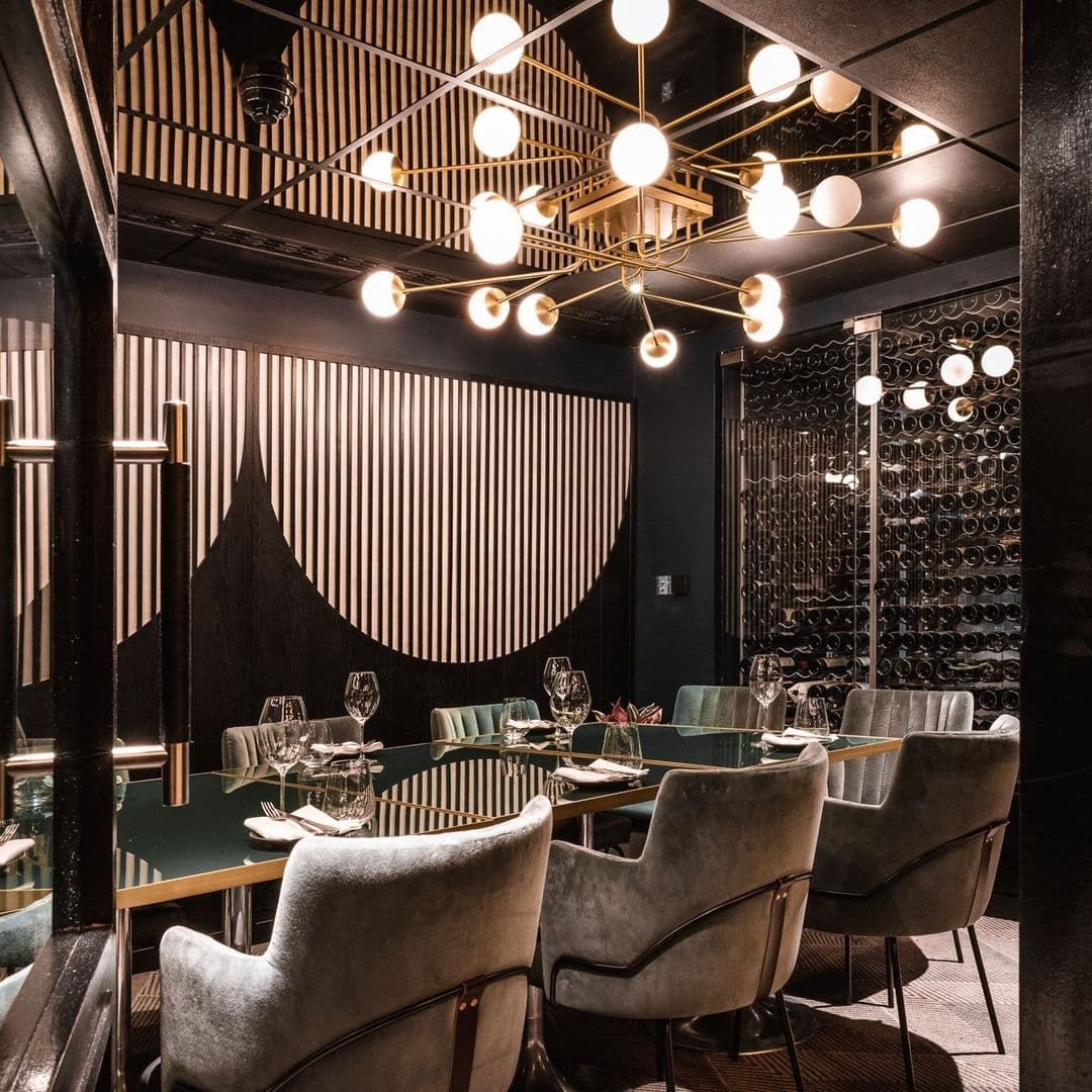 Elegant dining area at Gaucho with modern decor, featuring plush seating, geometric lighting fixtures, and a wall of wine bottles.