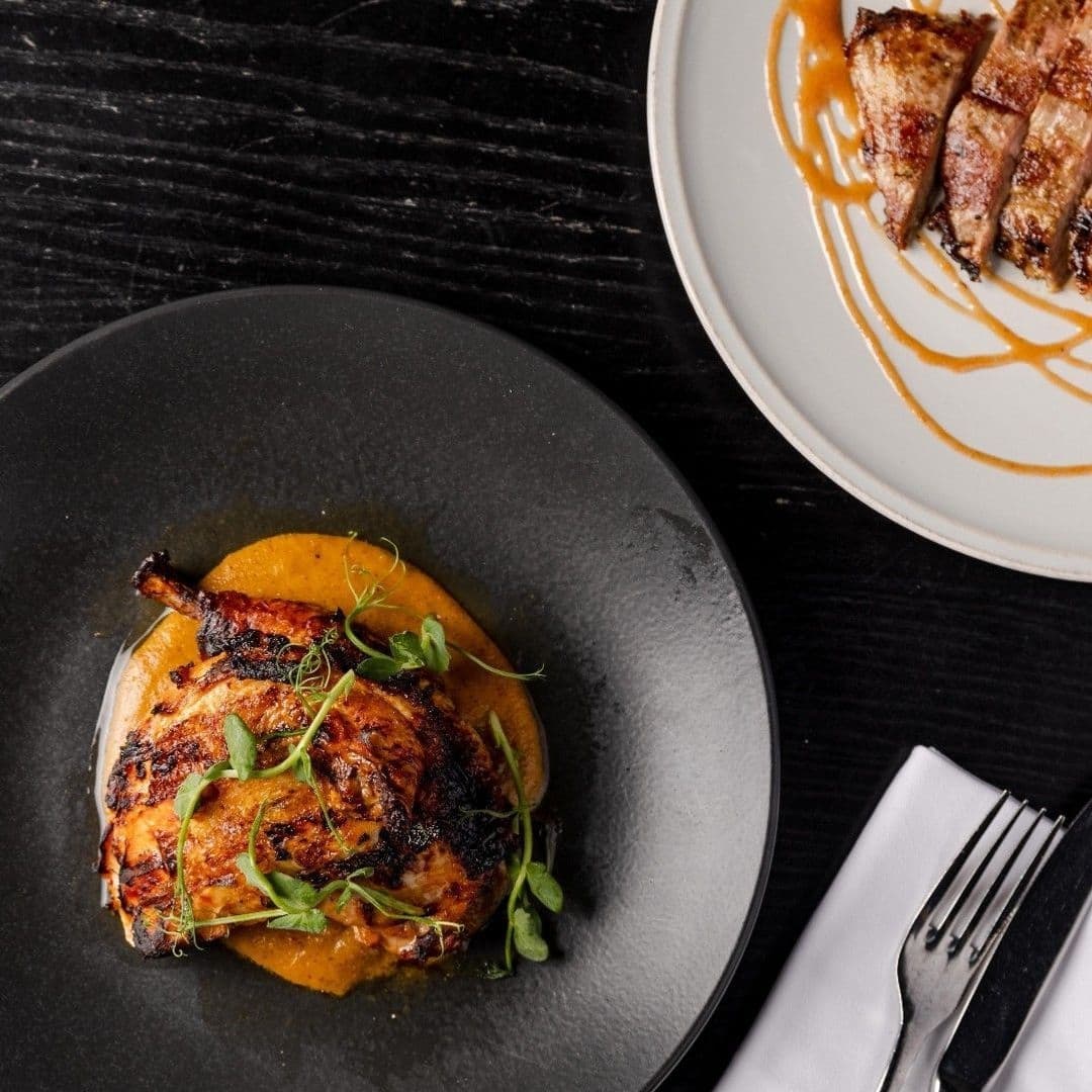 Grilled chicken dish served on a dark plate with a puree and garnished with greens at Gaucho restaurant.