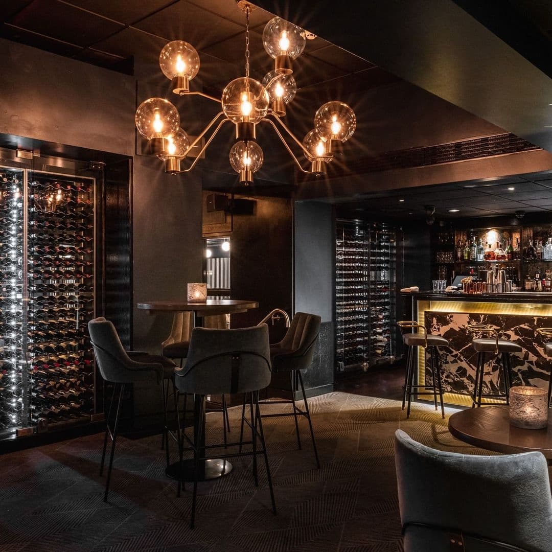 Elegant interior of Gaucho featuring modern bar with golden accents, stylish spherical chandeliers, and a wine rack wall.