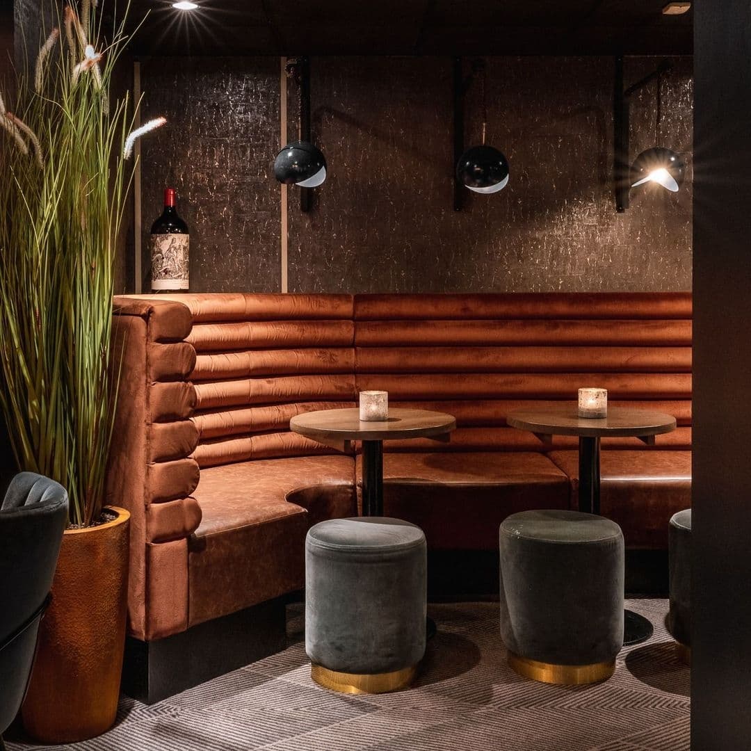 Cozy corner seating area at Gaucho with plush brown leather benches, round wooden tables, velvet stools, and ambient lighting.