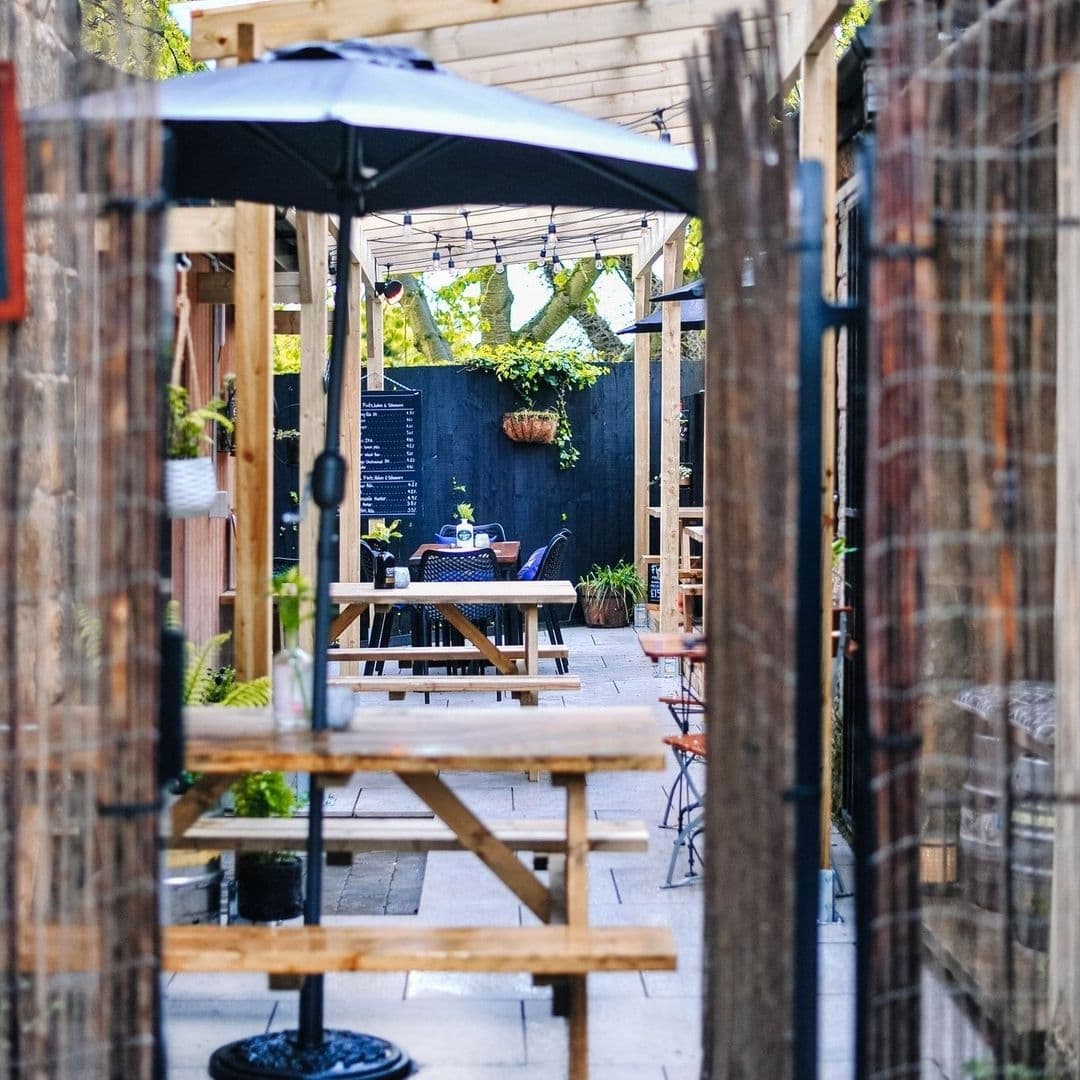 Cozy outdoor seating area at Granvilles Beer & Gin House with wooden tables, string lights, and greenery.