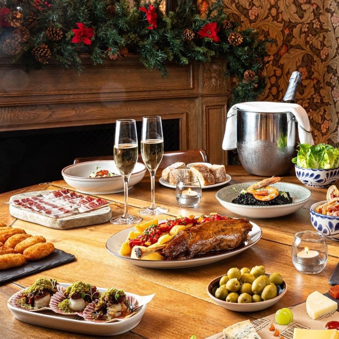 Gourmet dining experience at Ibérica with a variety of Spanish dishes, including cured meats, seafood paella, roasted lamb, and tapas, complemented by champagne and a festive atmosphere.