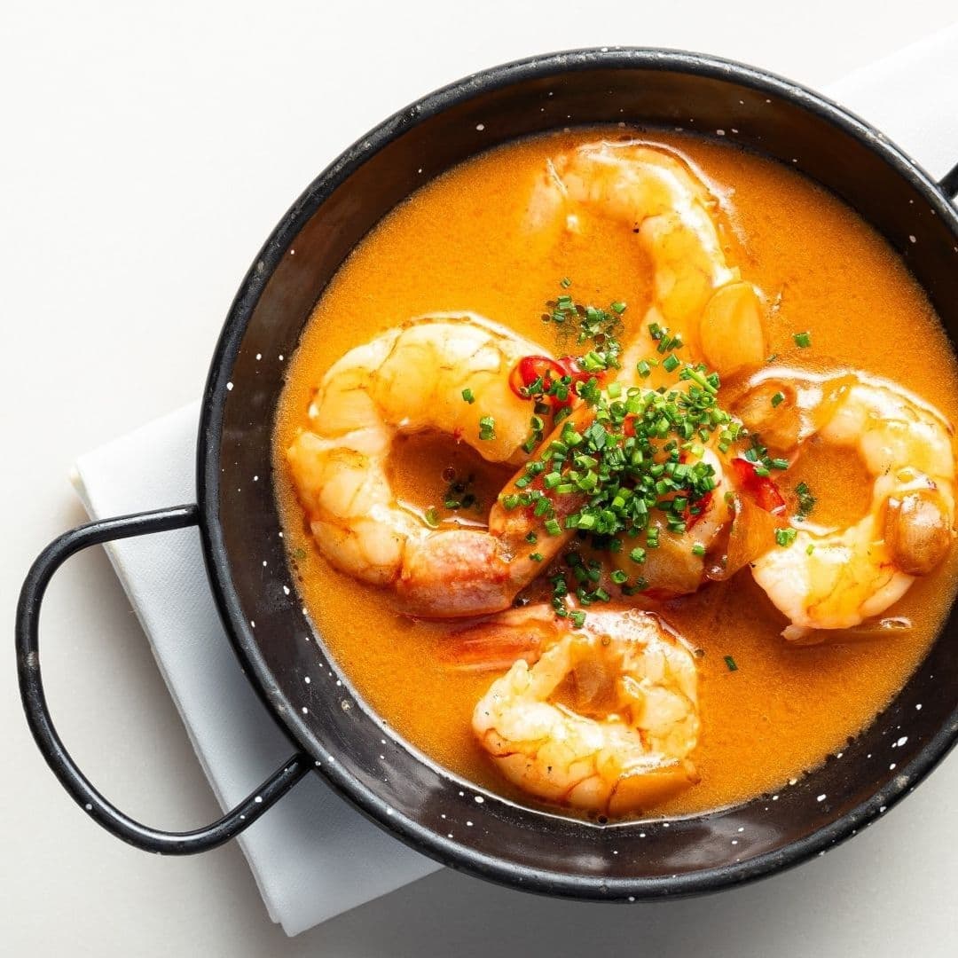 Traditional Spanish shrimp dish served in a black ceramic bowl, garnished with fresh herbs and red pepper, representing the culinary experience at Ibérica.