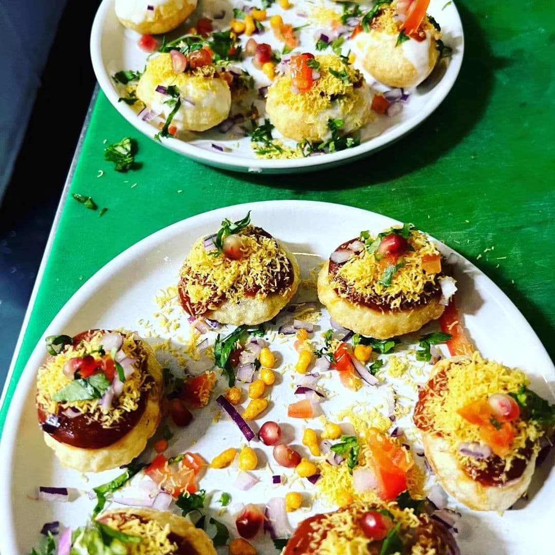 Plates of colorful Indian chaat featuring pani puri garnished with yogurt, sev, chopped onions, tomatoes, and coriander at Indian Pakwaan.