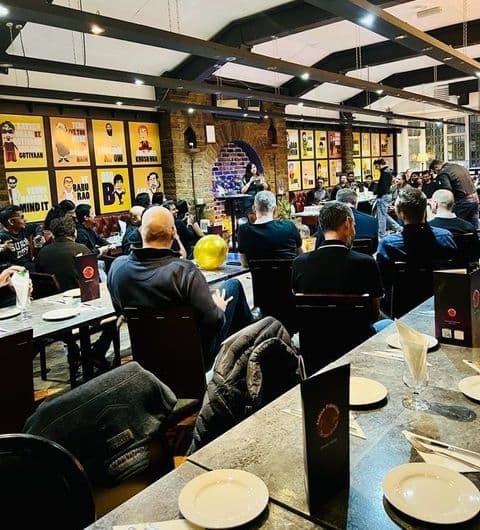 Interior of Indian Pakwaan restaurant with patrons seated at tables, colorful posters on the walls, and a lively atmosphere.