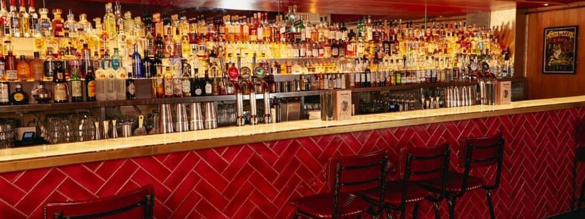 Interior of Jake's Bar & Still Room showing an extensive selection of spirits on backlit shelves, beer taps, and red bar stools.