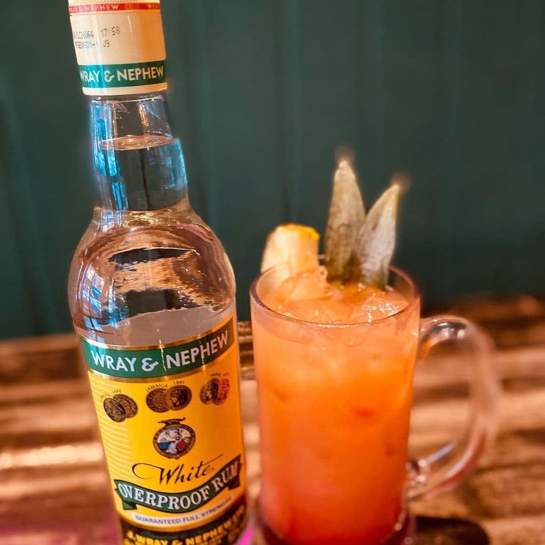 A bottle of Wray & Nephew White Overproof Rum next to a refreshing cocktail garnished with pineapple and leaves, representing the vibrant spirit of Jamrock.