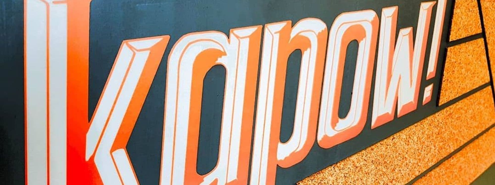 Close-up of the Kapow Coffee – The Calls sign with bold orange and white lettering on a dark background.