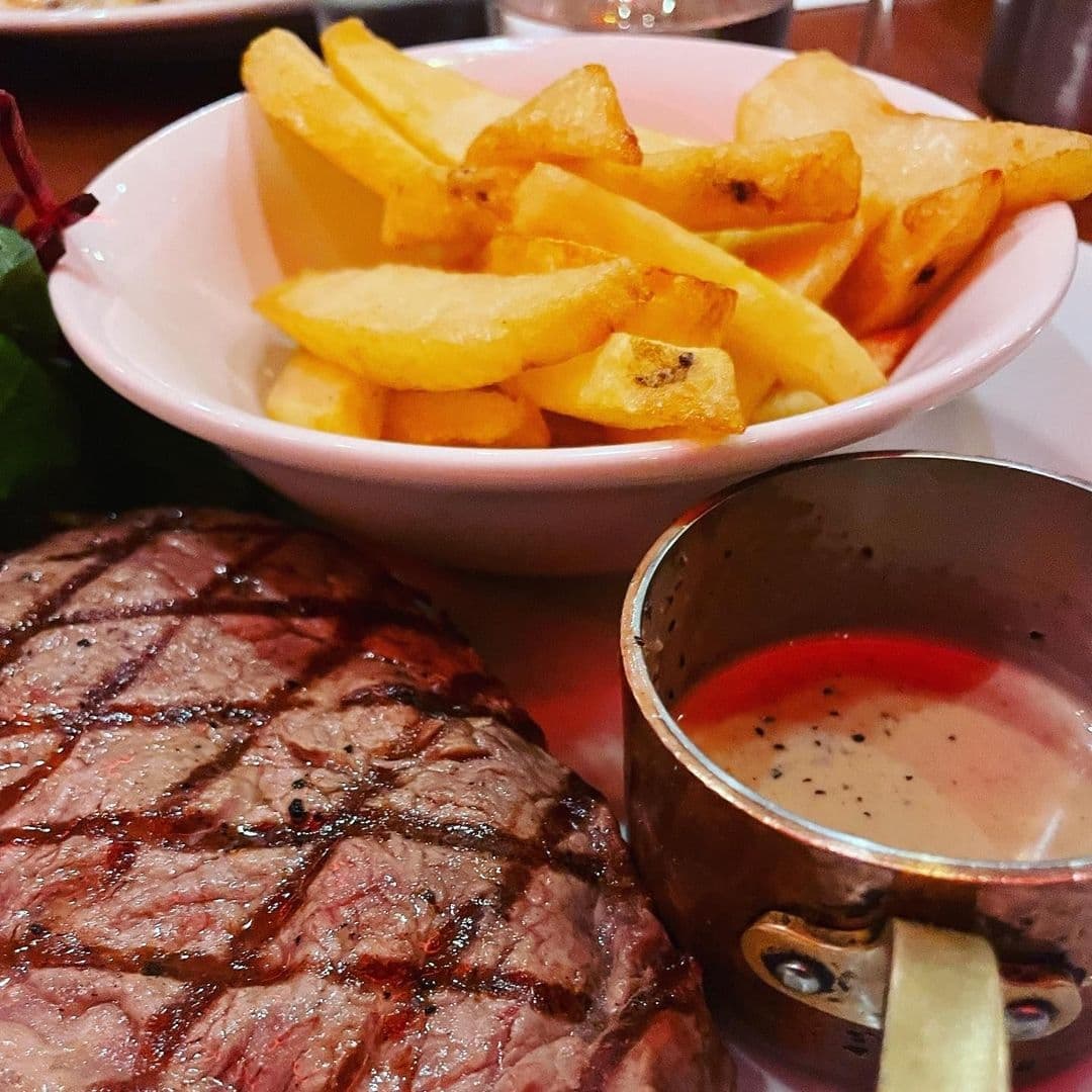 Grilled steak with grill marks served with a side of golden French fries and a small cup of sauce at Lavanta Meze Bar & Grill.