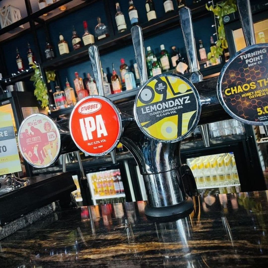 Beer taps featuring various craft beers on the polished counter of Mad Frans Bar, with a selection of spirits on shelves in the background.