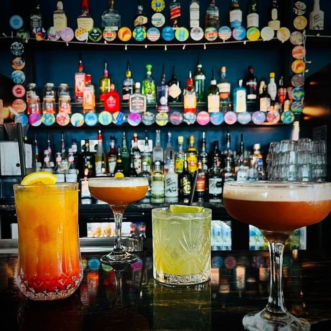 Colorful cocktails on the counter at Mad Frans Bar with a backdrop of assorted liquor bottles and decorative coasters.
