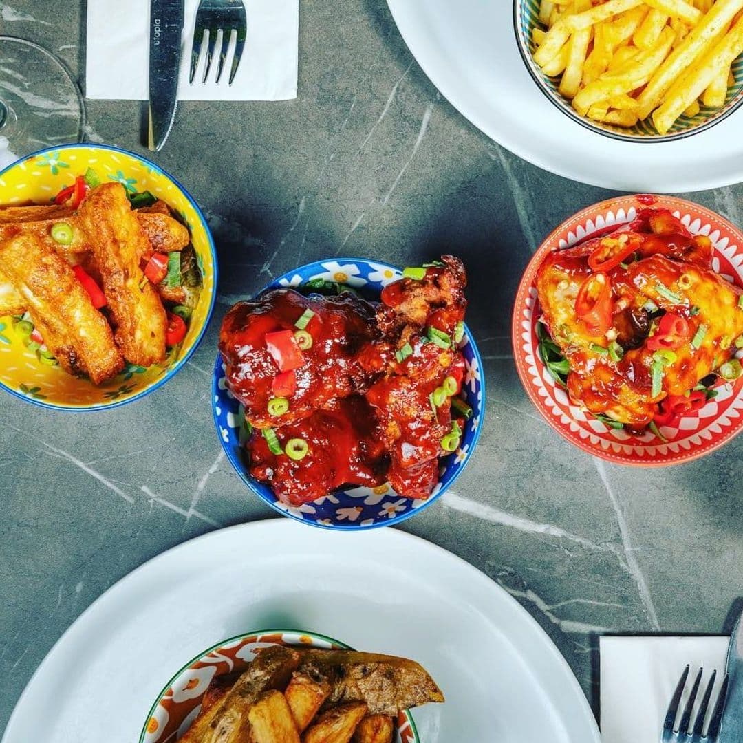 Assorted savory dishes at Mad Frans Bar, featuring glazed chicken wings, seasoned fries, and potato wedges served in colorful bowls on a marble table.