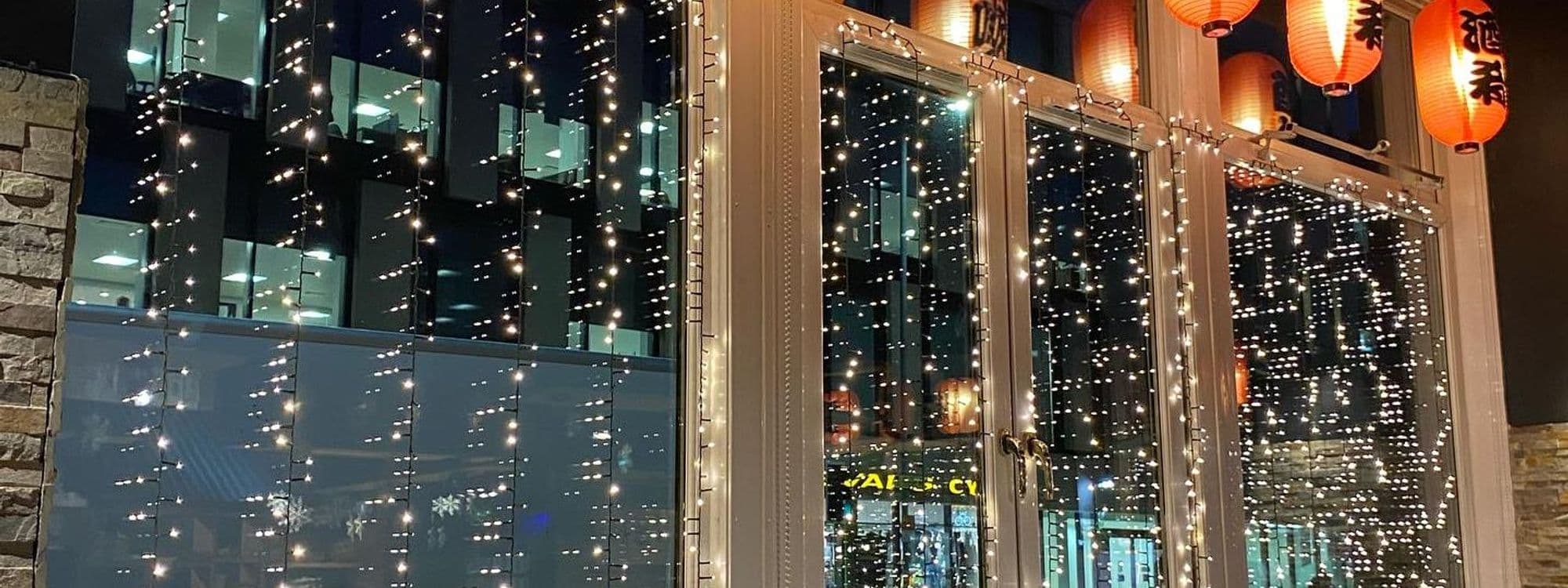 Exterior view of Maki & Ramen restaurant at night, adorned with twinkling string lights and traditional orange lanterns with Japanese characters.