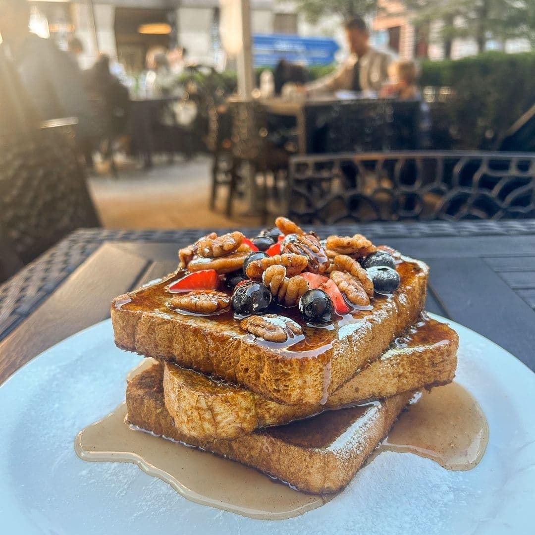 Plate of French toast topped with strawberries, blueberries, pecans, and syrup at Moose Coffee, with blurred background of restaurant patrons.