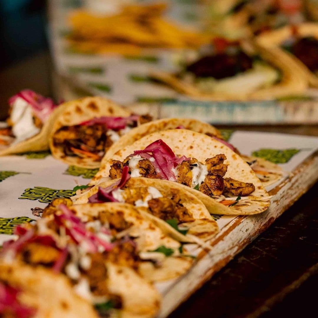 Assorted tacos on a wooden serving tray at Neon Cactus, featuring a variety of fillings and topped with fresh red onions and herbs.