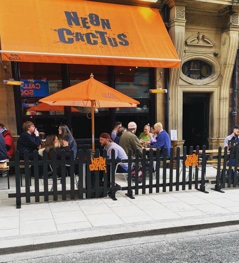 Outdoor seating area at Neon Cactus with patrons dining under an orange umbrella and a matching orange awning with the establishment's name.