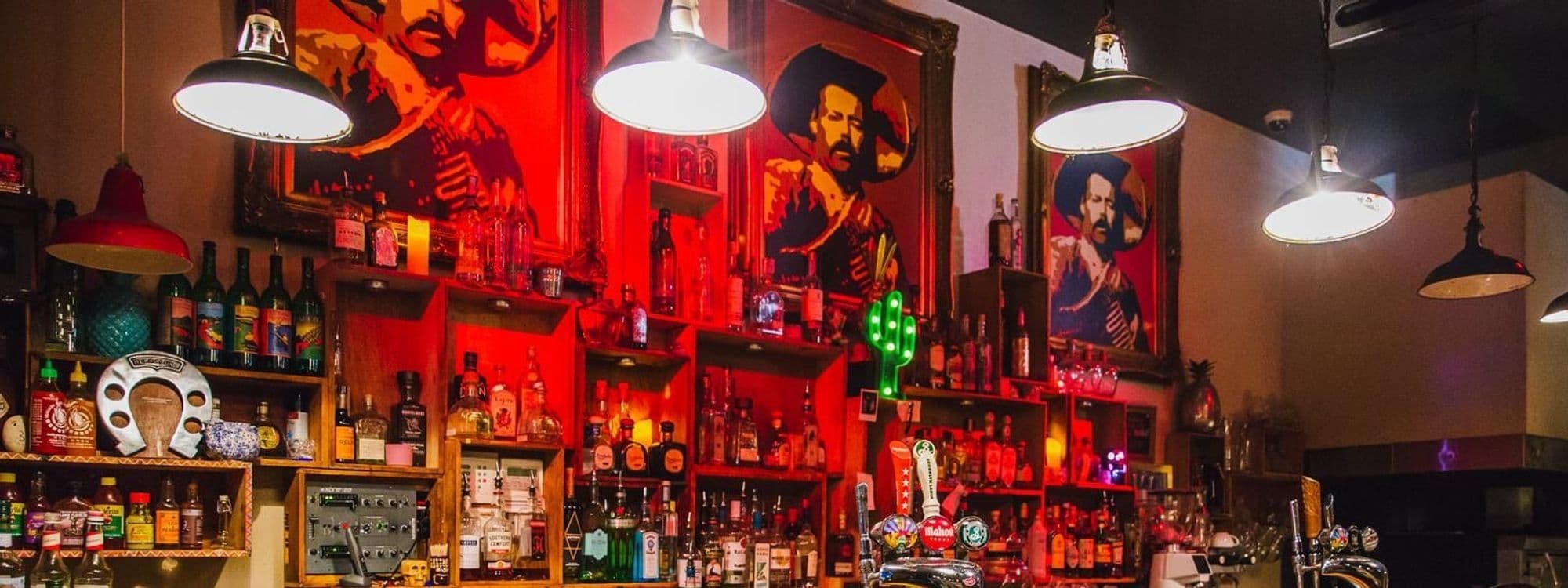Interior view of Neon Cactus featuring a vibrant bar with eclectic decor, assorted bottles, neon signs, and pop art portraits.