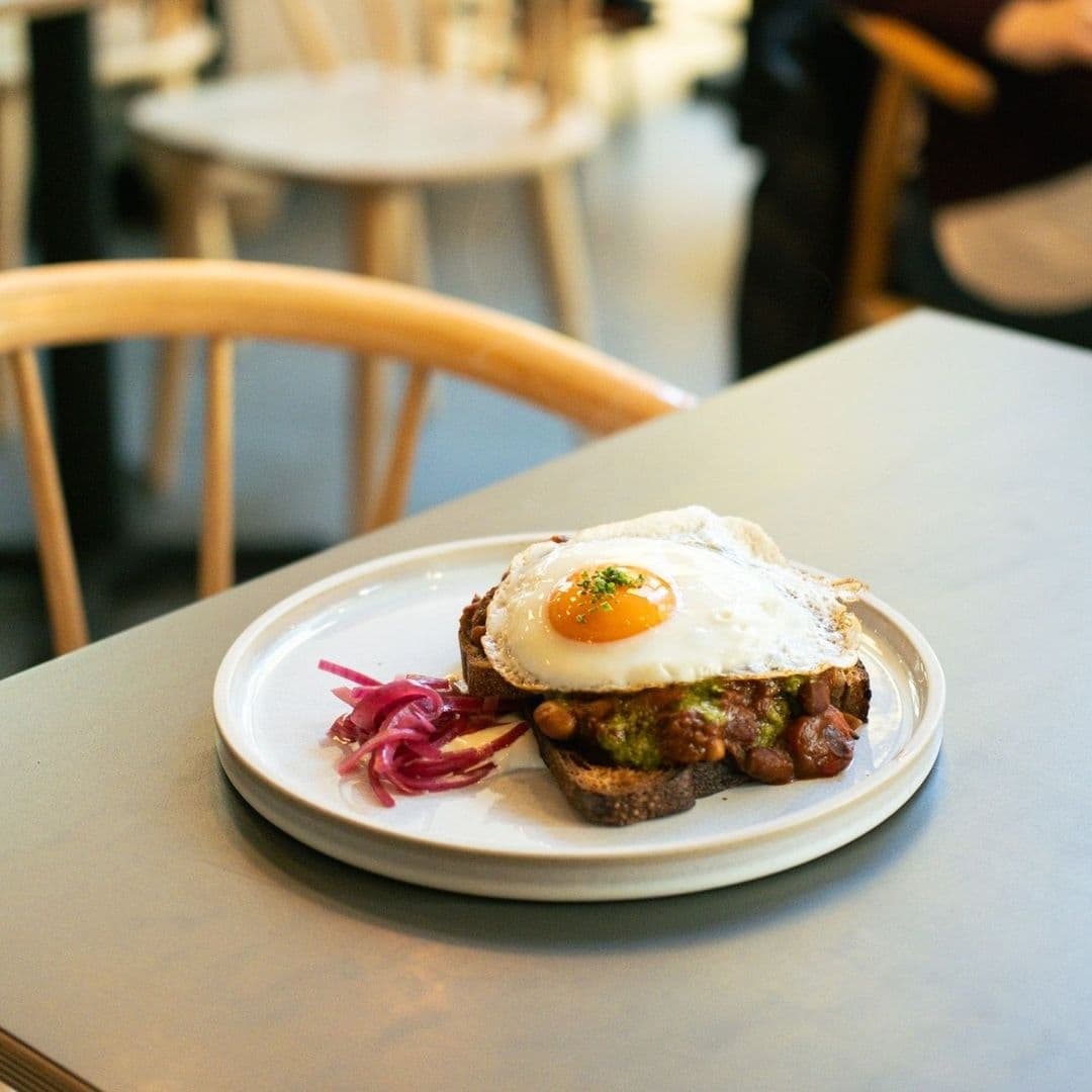Plate of avocado toast with a sunny-side-up egg and pickled onions at North Star Coffee Shop, with blurred background of cafe interior.