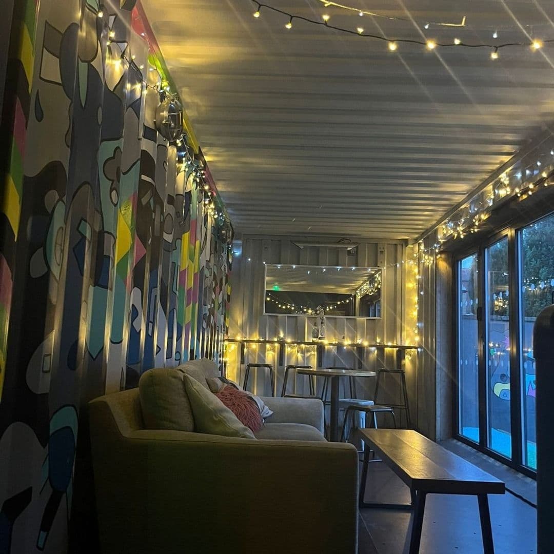 Cozy interior of Number Thirty Three featuring a comfortable green sofa with cushions, modern tables and chairs, and a vibrant graffiti-style wall mural. The space is warmly lit with twinkling string lights, creating an inviting atmosphere.