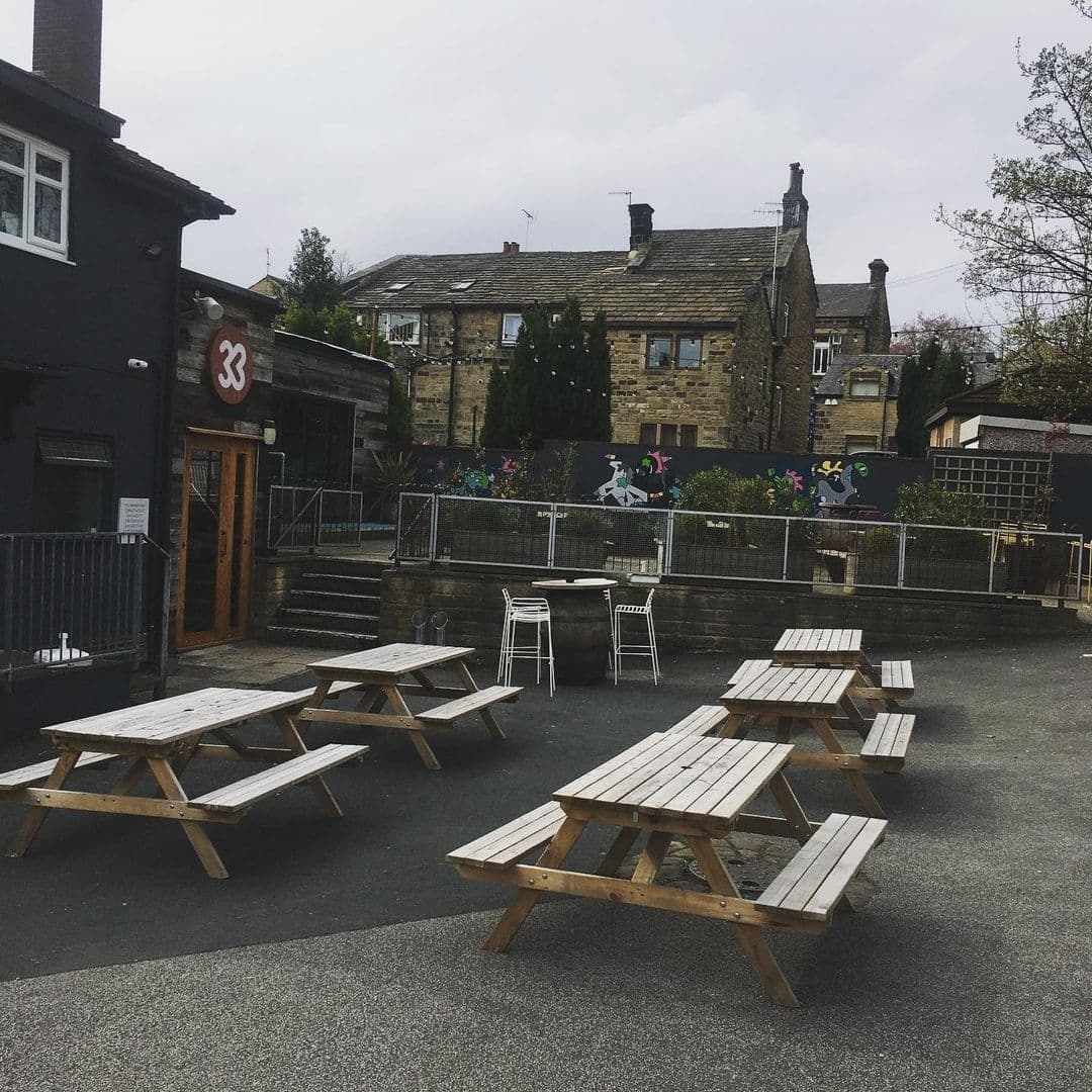 Outdoor seating area at Number Thirty Three with wooden picnic tables on a paved patio, adjacent to a building with a large '33' sign.