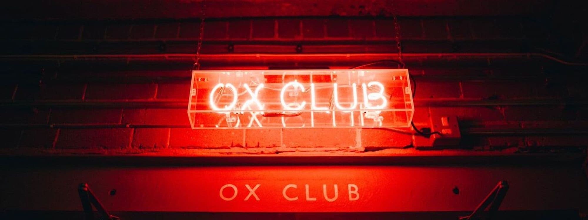 Neon sign of Ox Club at Headrow House glowing in red against a brick wall background.
