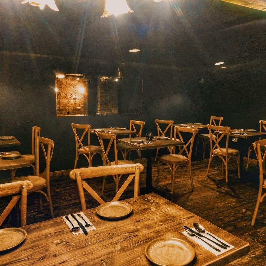 Cozy dining area at Phranakhon with wooden tables and chairs, set for a meal under warm lighting, and rustic wall decor.