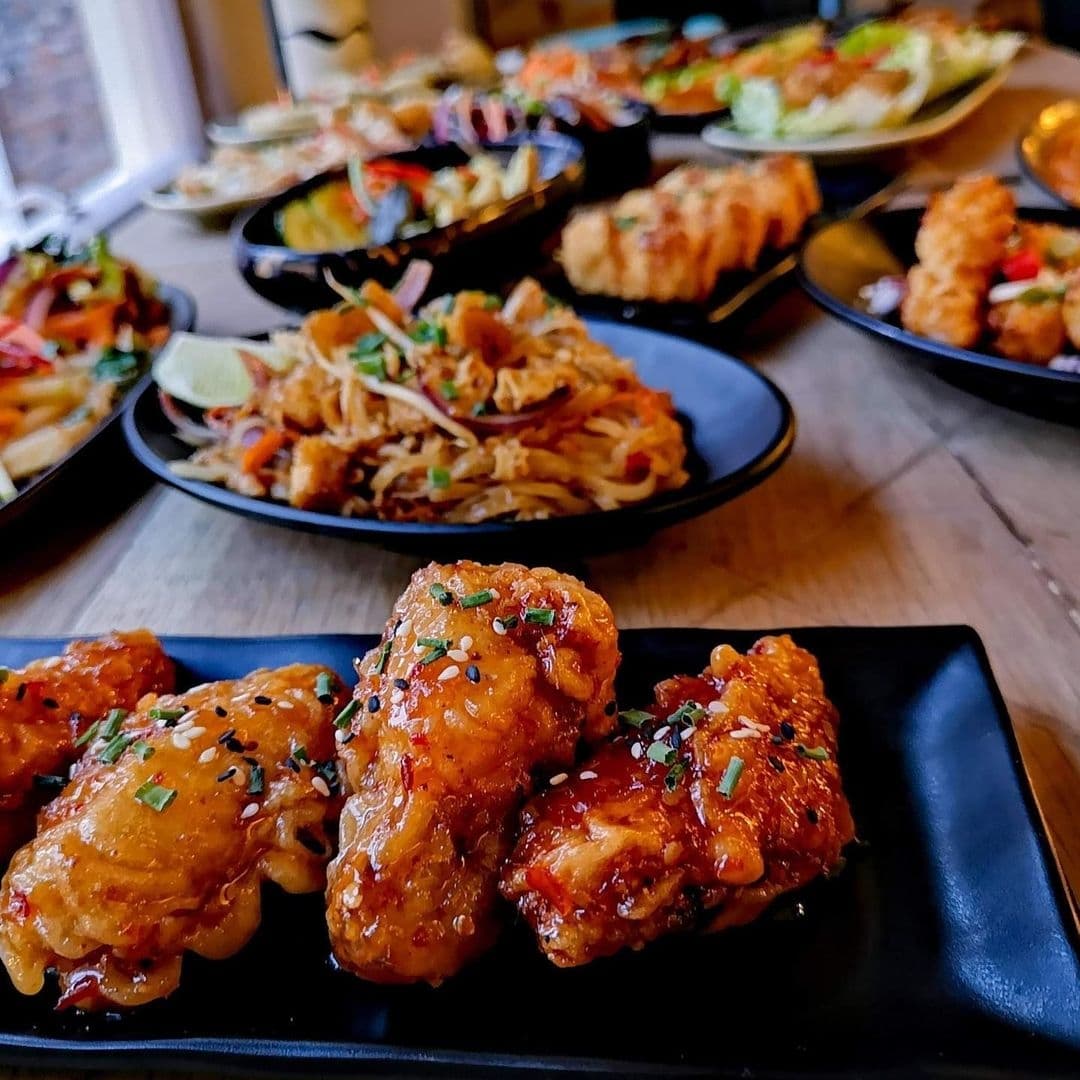 Assorted Thai dishes with focus on glazed chicken wings garnished with sesame seeds and green onions, served at a restaurant in Phranakhon.