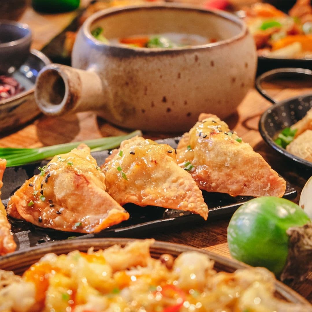 Alt text: "Delicious traditional Thai cuisine at Phranakhon, featuring crispy fried dumplings on a black plate, with a clay pot of soup and various other dishes in the background."