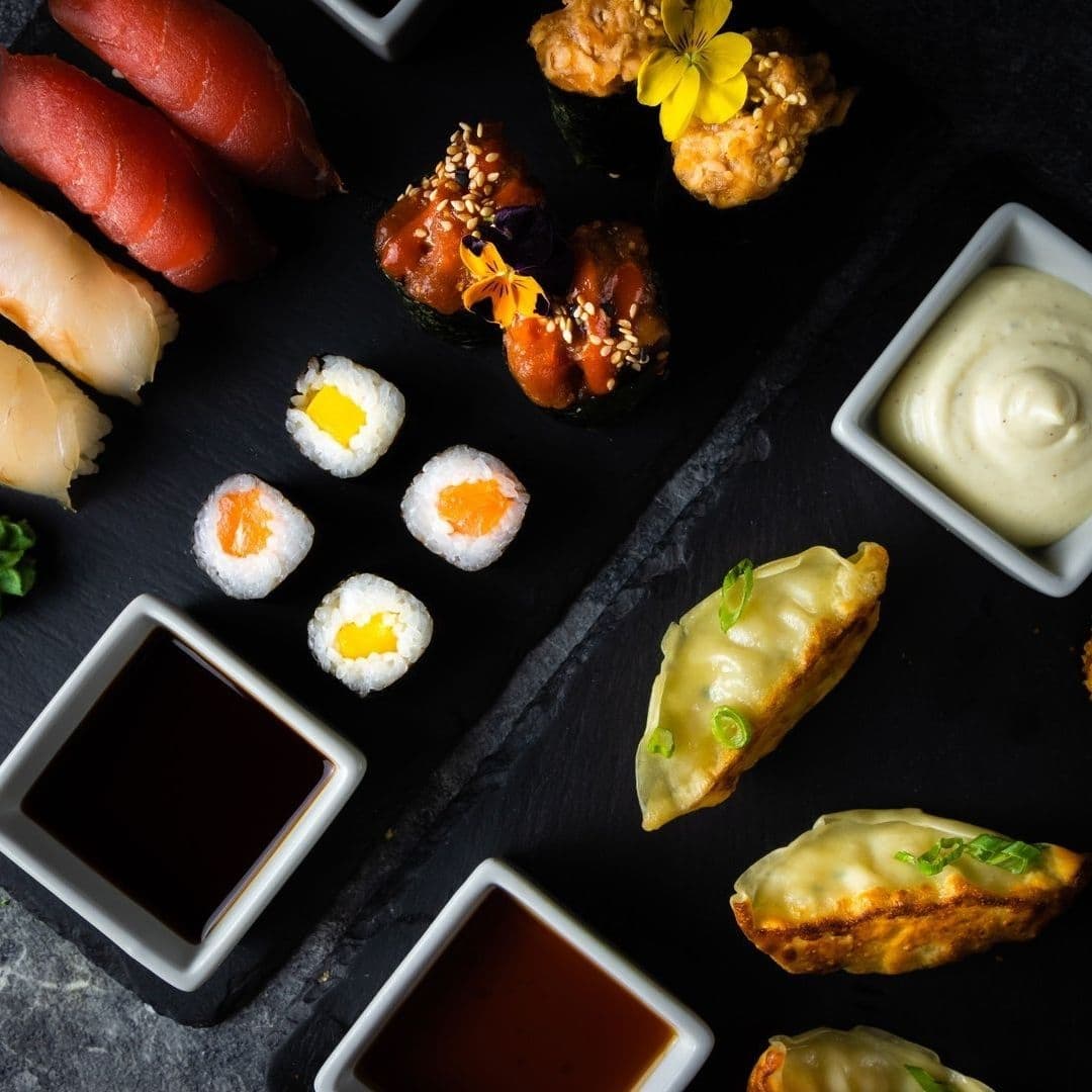 Assorted sushi and dumplings served with dipping sauces on a dark slate surface at Sakku.