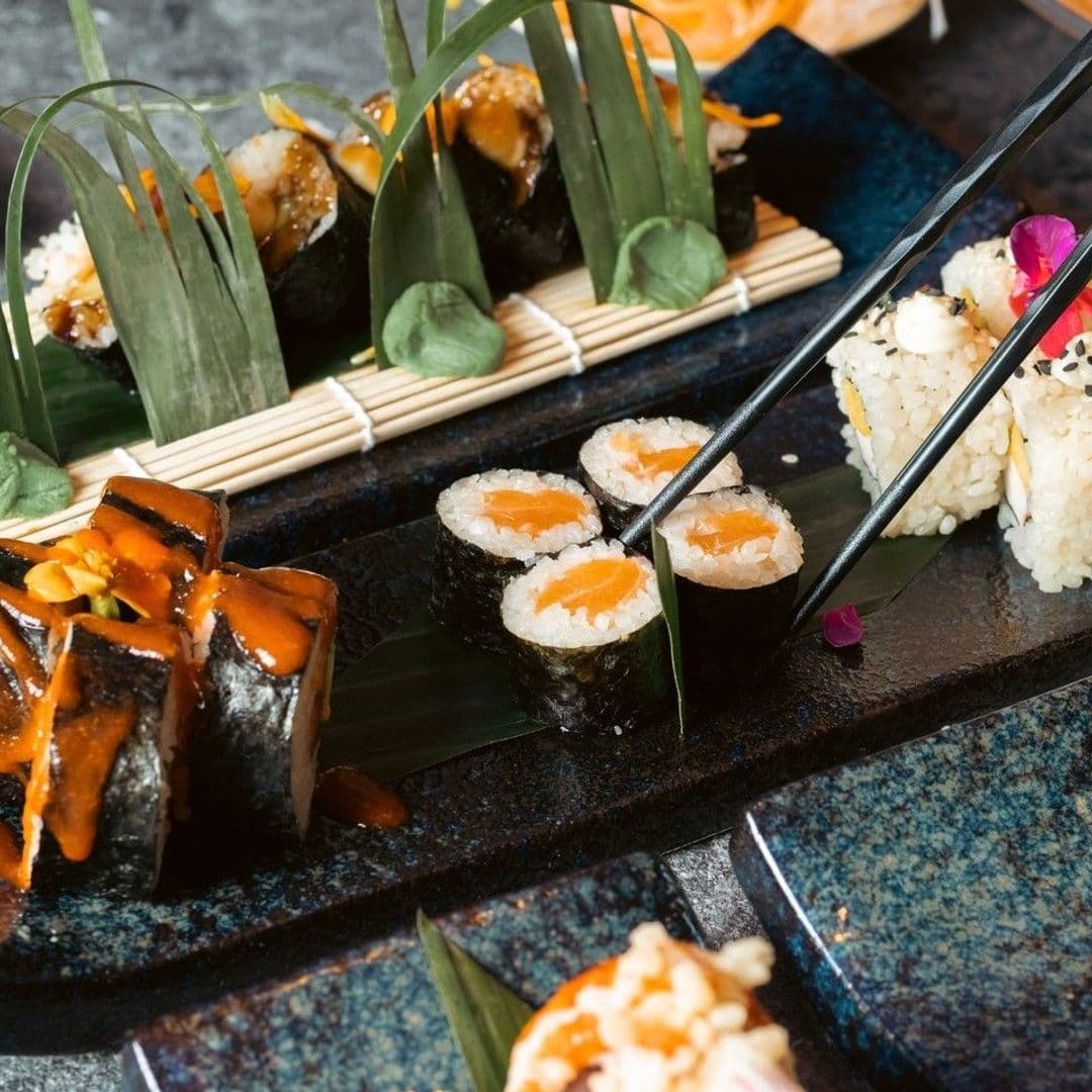 Assorted sushi selection on a dark plate at Sakku, featuring rolls with salmon and avocado garnished with edible flowers and green leaves.