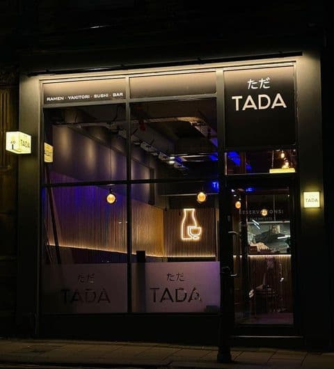 Exterior night view of TADA restaurant with illuminated signage, showcasing ramen, yakitori, sushi, and bar offerings.