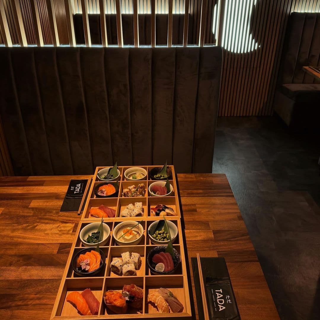 Assorted sushi and sashimi platter on a wooden table at TADA restaurant, with elegant interior lighting and modern decor.