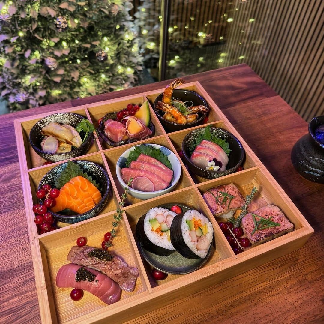 Assorted sushi and sashimi platter displayed in a wooden box at TADA, with a festive Christmas tree in the background.