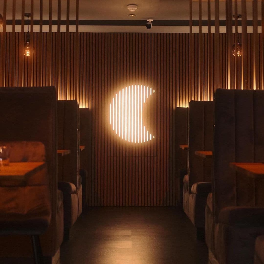 Interior of TADA with ambient lighting, featuring high-back chairs and a stylish wooden slat wall with a circular illuminated cutout.