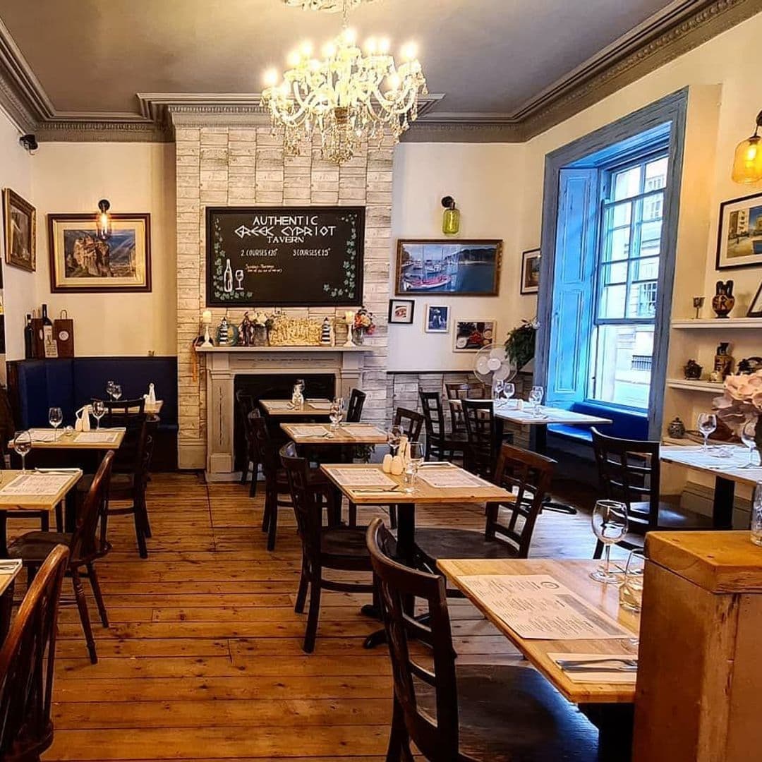 Interior of Tavernaki Bistro featuring wooden tables set for dining, a chandelier, and a blackboard advertising authentic cuisine.