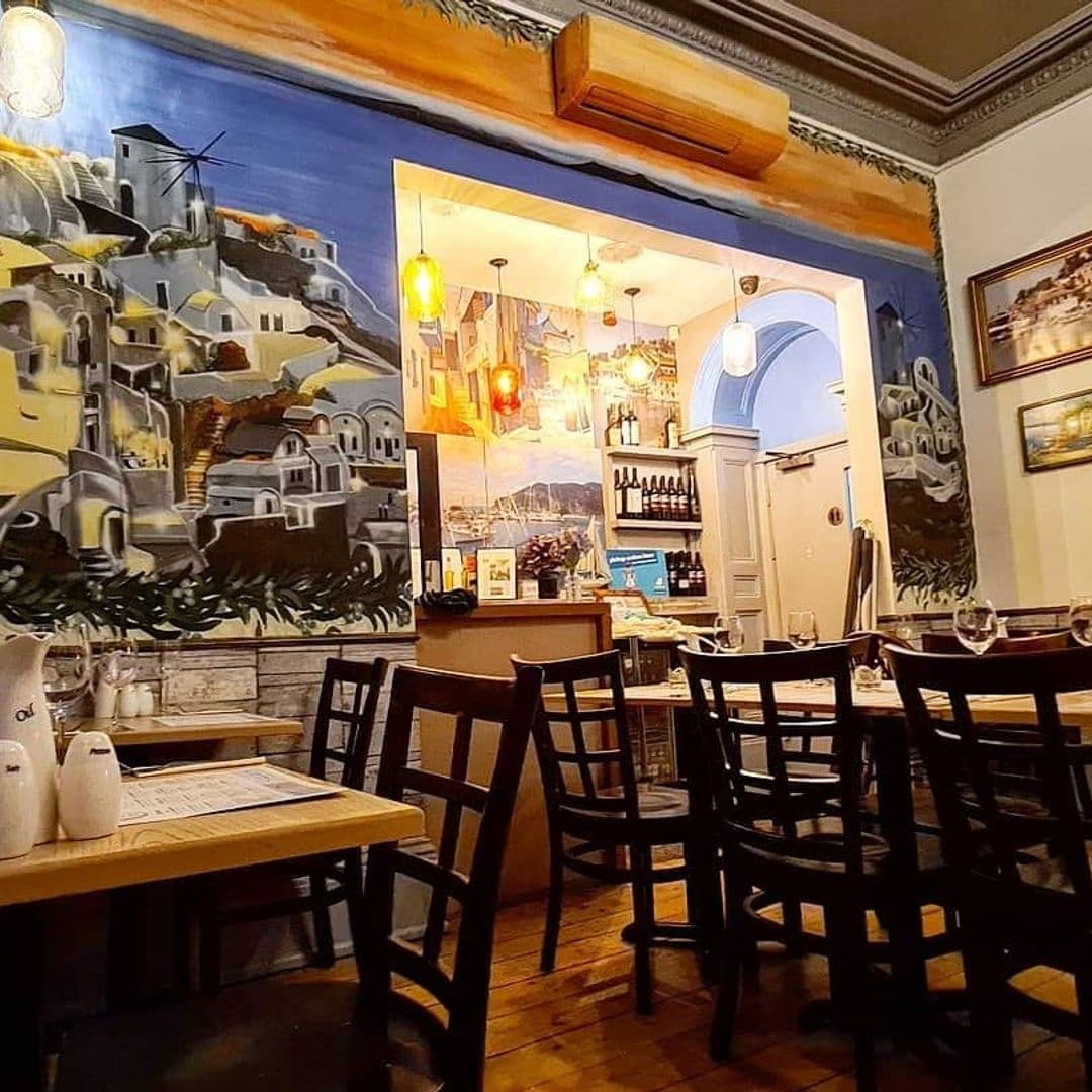 Interior of Tavernaki Bistro with wooden tables and chairs, Mediterranean-style murals on the walls, and warm lighting.