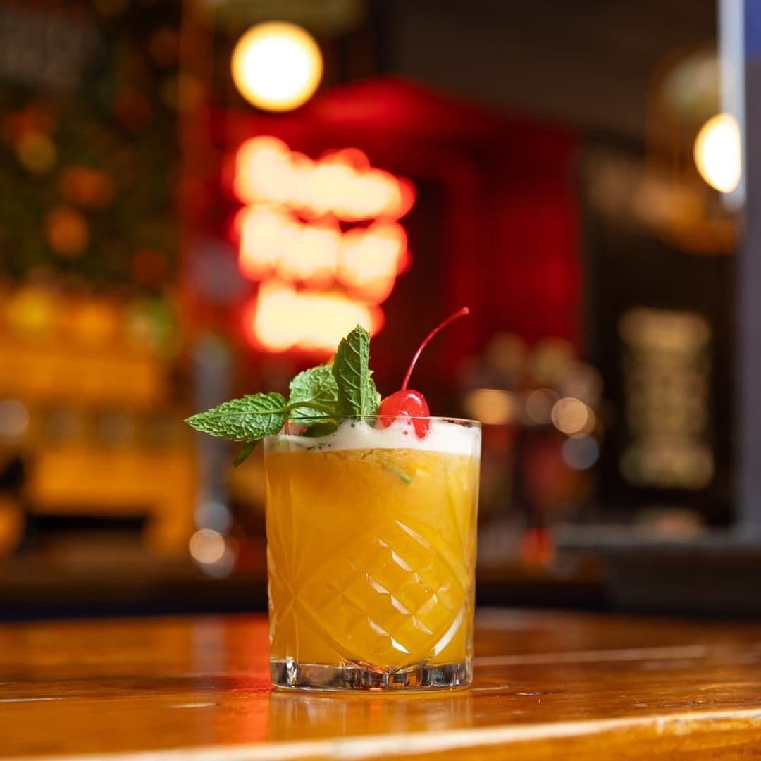 Refreshing cocktail with mint and cherry garnish on a wooden bar counter at The Bower's Tap, with warm ambient lighting in the background.