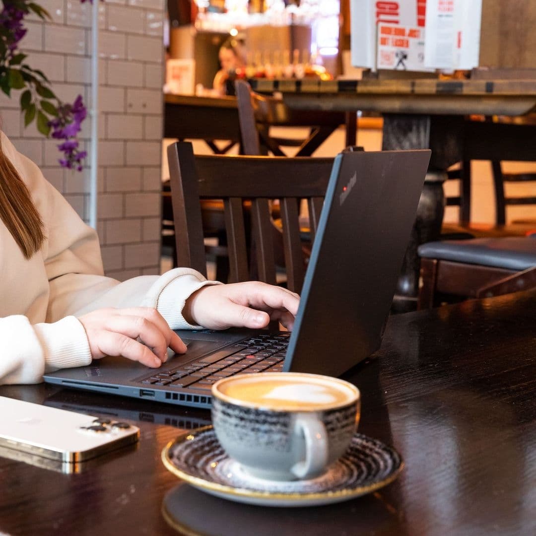 Person working on a laptop at The Bower's Tap with a cup of coffee and a smartphone on the table.