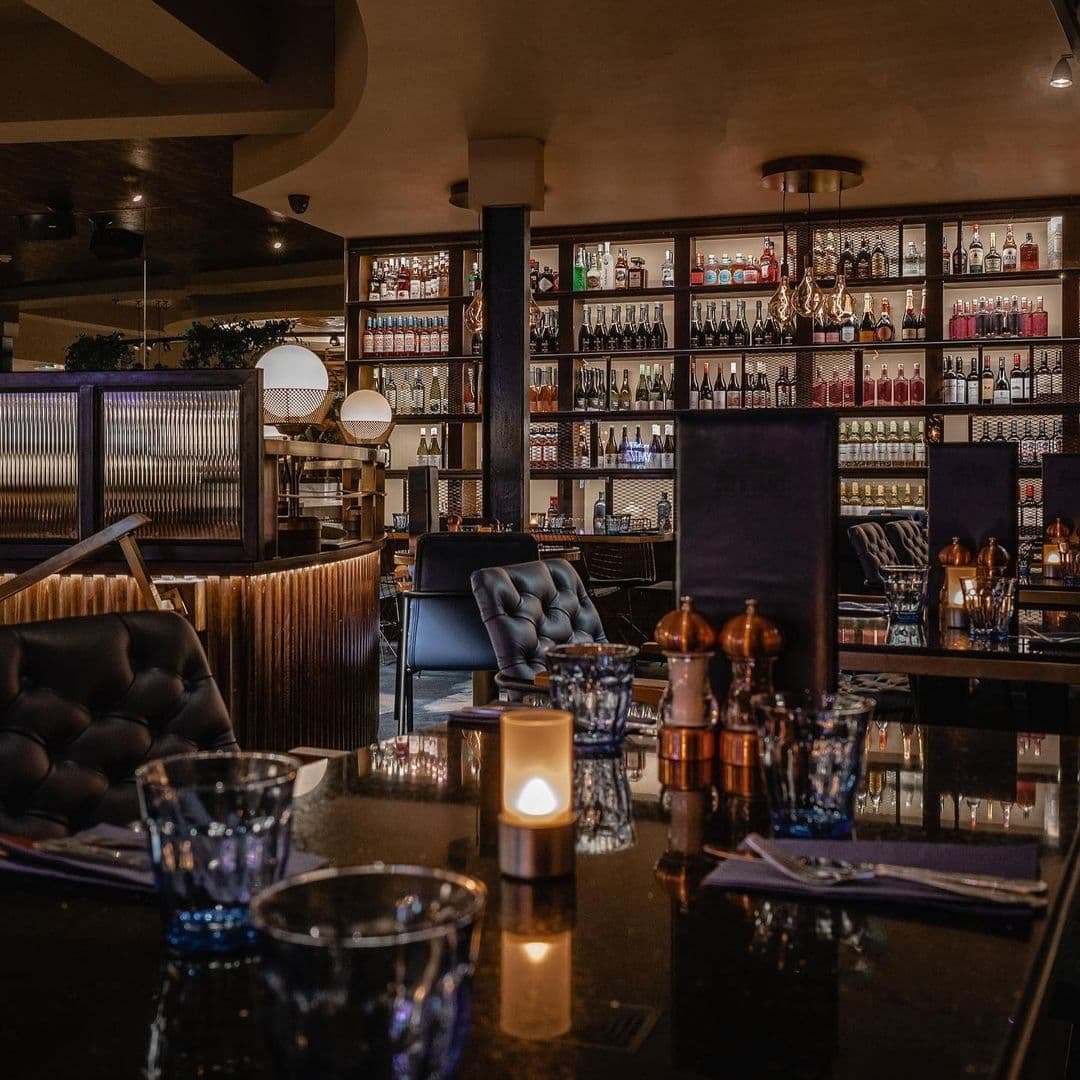 Interior of The Cut & Craft, showcasing a sophisticated bar area with an extensive selection of bottles on shelves, elegant furnishings, and warm ambient lighting.