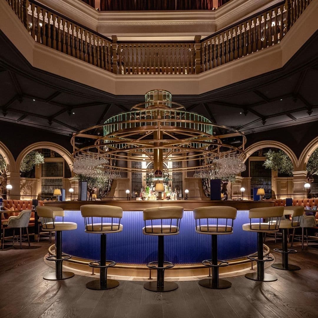 Elegant interior of The Cut & Craft featuring a central circular bar with blue lighting, surrounded by high stools, and an upper balcony with wooden balustrades.